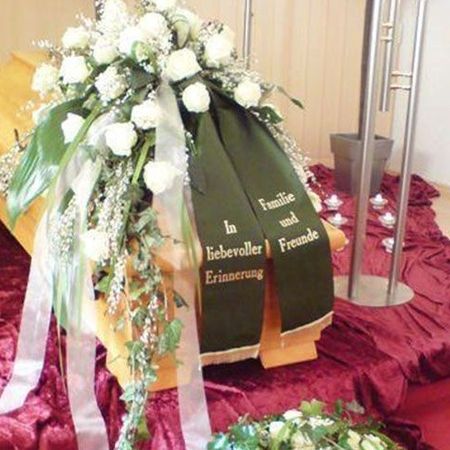 Blumenarrangement gehalten in weiß und grün mit gleichfarbigen, teilweise bestickten Schärpen