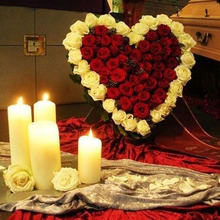 Von Kerzen erleuchtetes Herz, bestehend aus roten und weißen Rosen neben einem Sarg