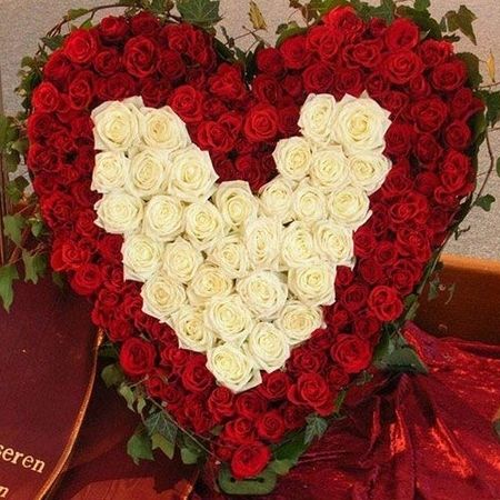 Üppiges Blumengesteck in Form eines Herzens bestehend aus roten und weißen Rosen mit bestickter Schärpe an der Seite