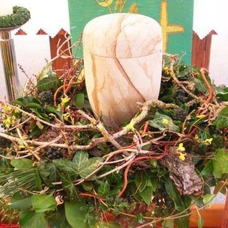 Urne mit Holz-Optik inmitten eines naturalen Kranzes verziert mit feinen Ästen und grünem Beiwerk