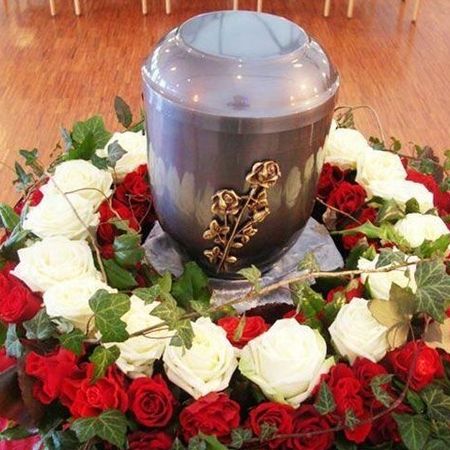 Anthrazitfarbene Urne in der Mitte eines Blumenkranzes aus weißen und roten Rosen thronend