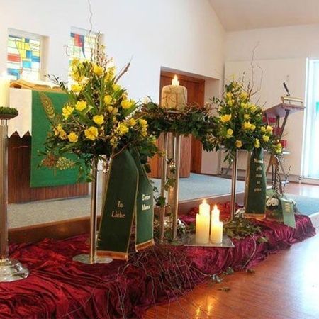 Trauergestecke mit gelben Blumen und grünen, bestickten Schärpen zwischen Kerzenständern