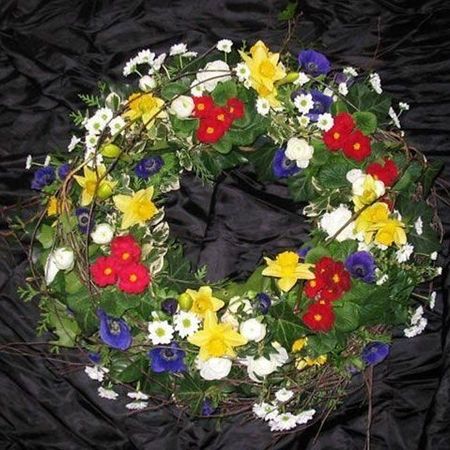 Trauerkranz mit roten, weißen, blauen und gelben Blumen drapiert auf schwarzem Stoff