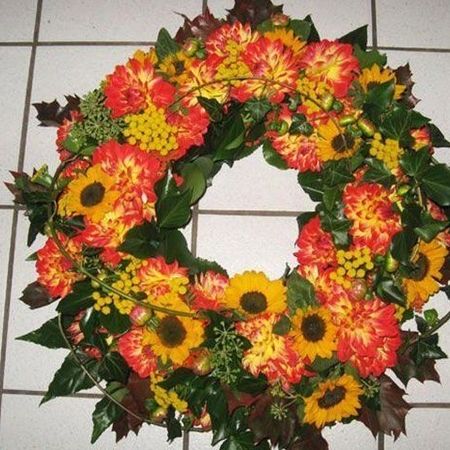 Trauerkranz mit Blumen in rot und orange gehalten sowie üppigem, dekorativem und grünem Beiwerk