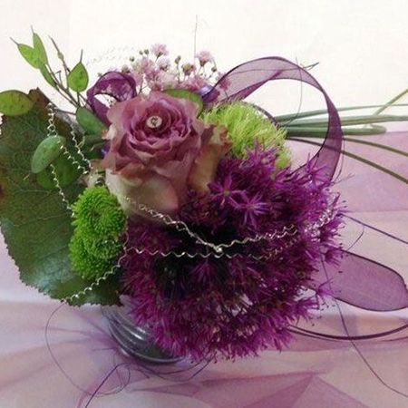 Festliche Zusammenstellung weißer und violetter Blumen mit schmückendem Beiwerk in einer kleinen Vase dekorativ auf einem Stofftuch präsentiert