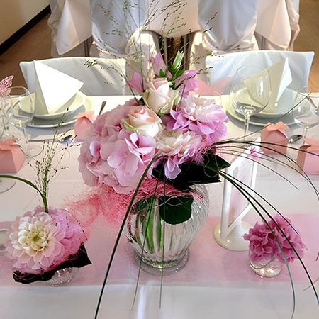 Elegantes Arrangement weißer und rosaroter Blumen mit filigraner Dekoration in einer Vase in der Mitte von zwei kleineren Blumenzusammenstellungen in gleicher Farbwahl
